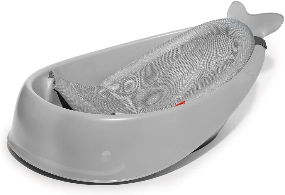 Baby in a shark-shaped bathtub with a person assisting