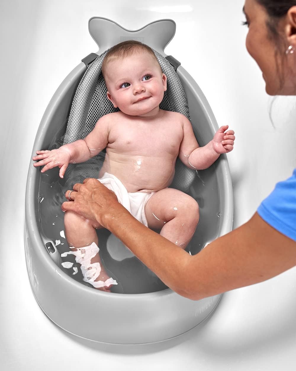 Baby in a shark-shaped bathtub with a person assisting