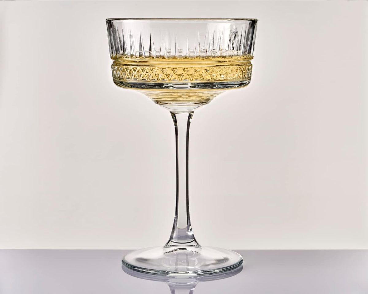 Clear glass coupe with gold rim on a light gray background