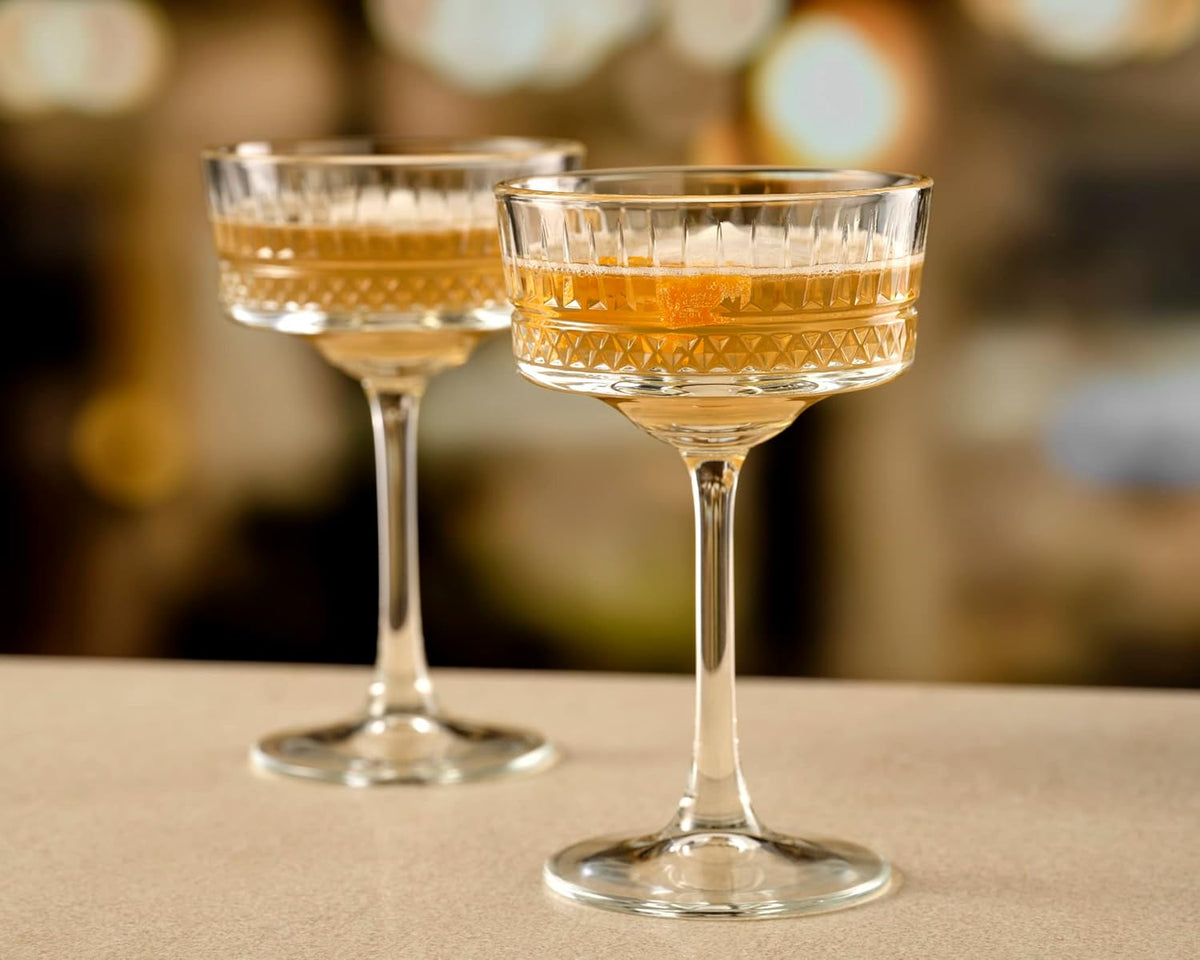 Two cocktail glasses with a golden liquid on a blurred background