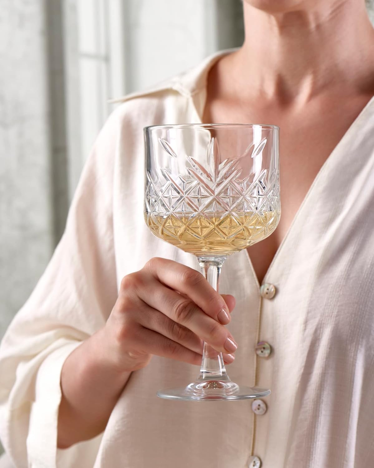 Person holding a crystal wine glass with white wine against a neutral background