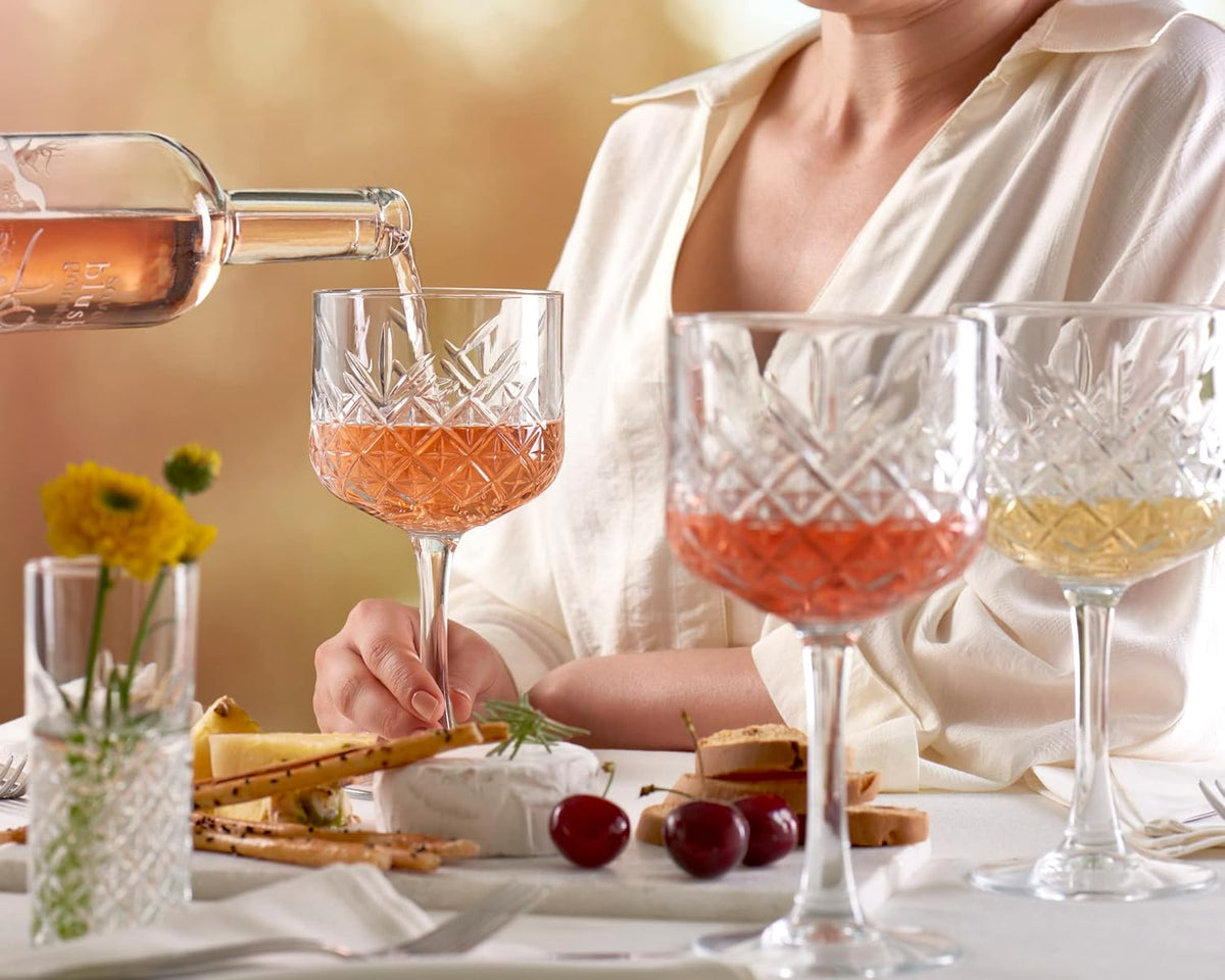 Person pouring rose wine into a glass with a table setting in the background