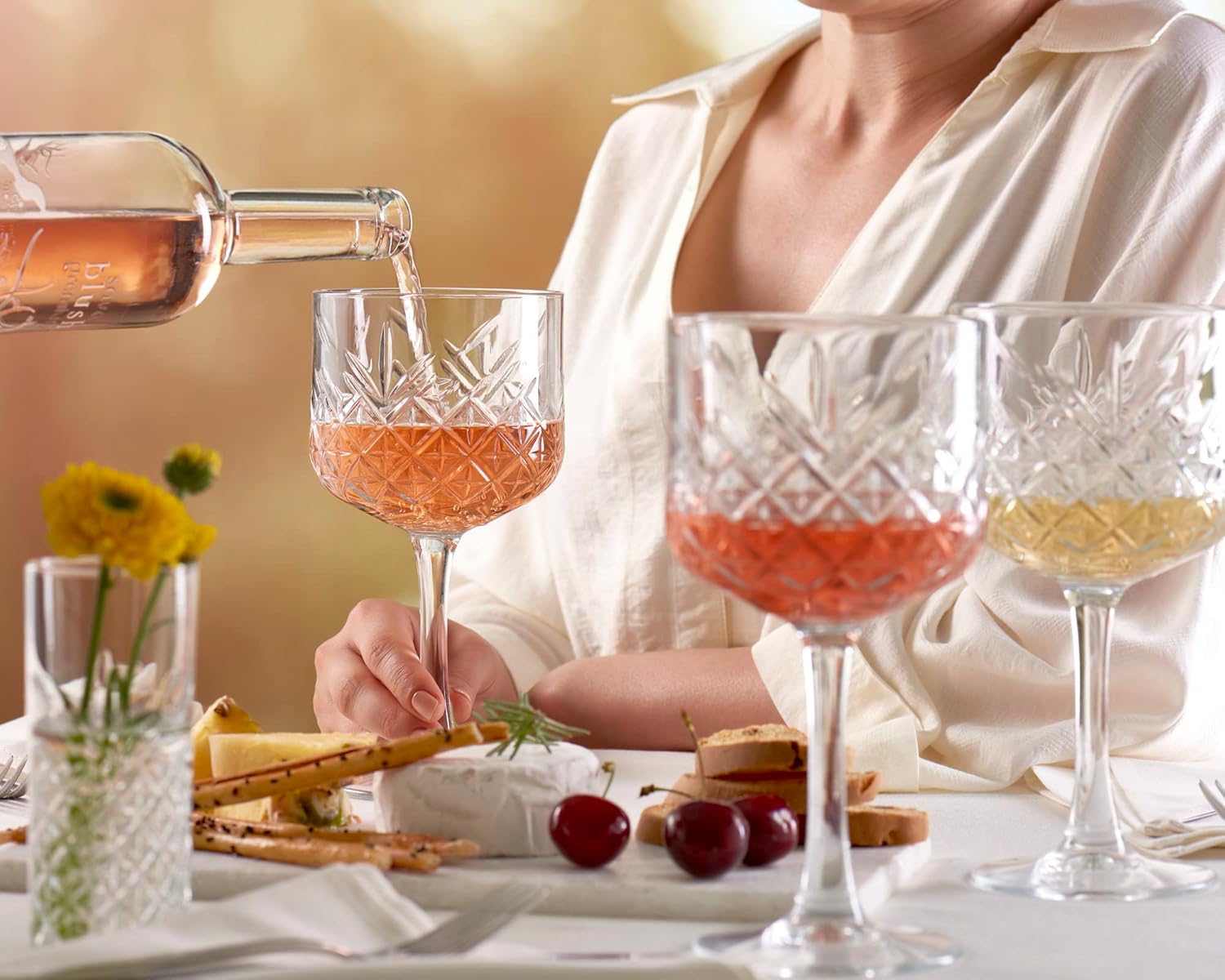 Four glass goblets with different colored liquids on a table with a person partially visible.
