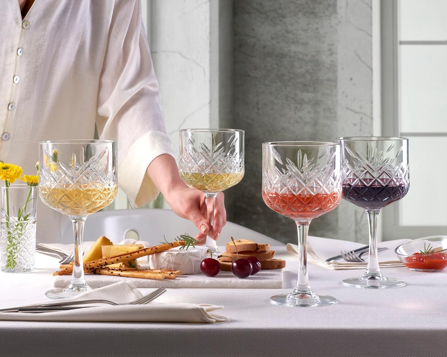 Four glass goblets with different colored liquids on a table with a person partially visible.